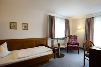 Beispielzimmer mit Bett, gemütlicher Leseecke und Schreibtisch