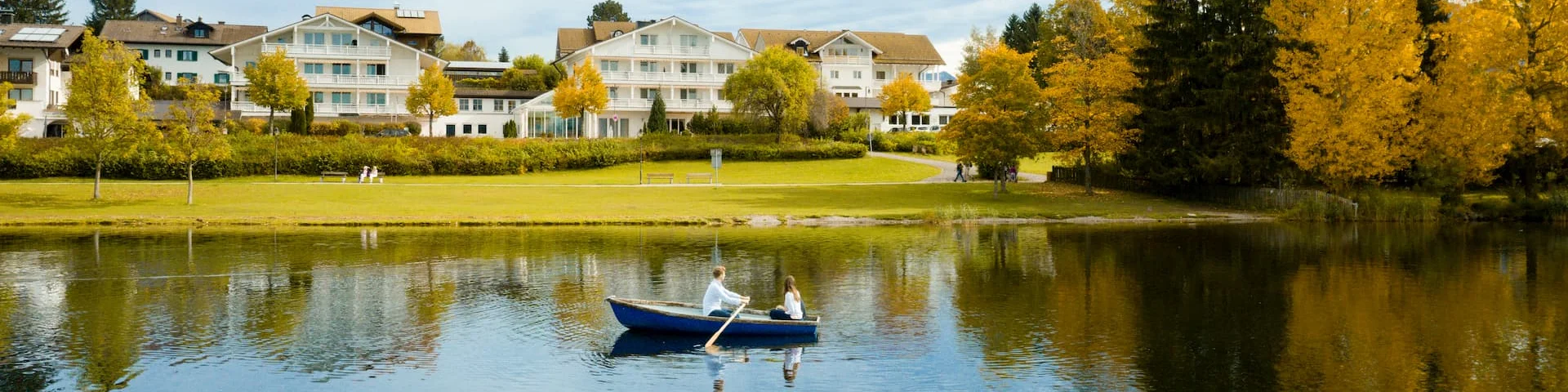 das Kneipp-Sanatorium Möst aus dem Hopfensee heraus fotografiert - ein Ruderboot mit Pärchen im Verdergund