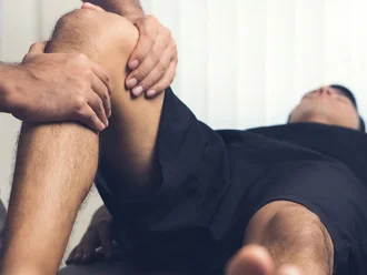 Person wird von jemandem am Knie therapiert