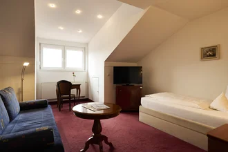 Beispielzimmer mit gemütlichem Bett, Sitzecke und Tisch. Kommode mit TV drauf